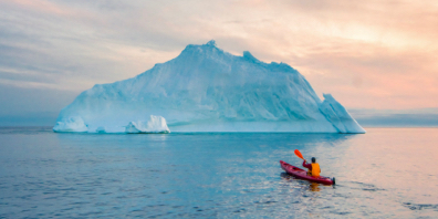 A lone kayaker paddles towards an iceberg